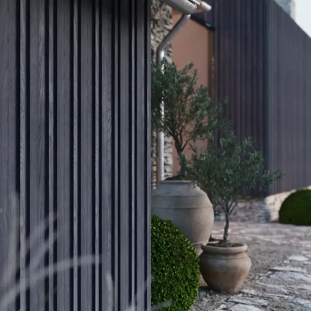 Bardage Millboard anthracite en pose verticale avec pots décoratifs, illustrant une façade moderne et durable dans un jardin méditerranéen.