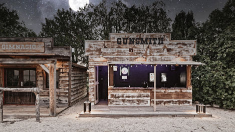The shooting range at Mas de Campe, featuring a wooden "Gunsmith" booth and a high-end electronic dartboard. The booth is styled like an old Western storefront, adding to the unique charm of the area