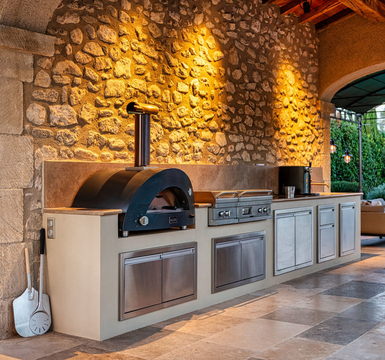 Cuisine extérieure sur-mesure en pierre avec four à pizza et plancha intégrés, combinant matériaux nobles et équipements haut de gamme pour une cuisine en plein air