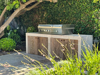 Grill gaz Lacanche installé dans une cuisine d’été sur mesure en pierre naturelle et bois, au cœur d’un jardin méditerranéen.