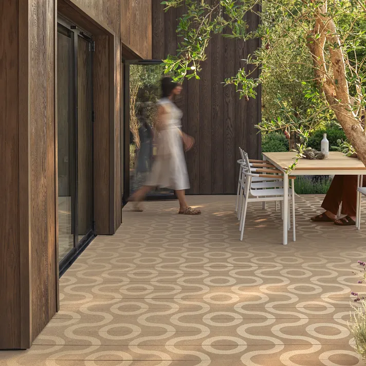 Espace repas extérieur en bois clair avec sol en bois composite clair à motif circulaire, ambiance méditerranéenne douce.