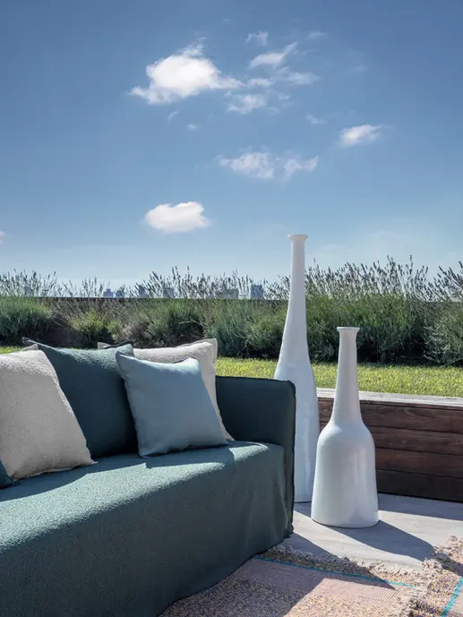 Canapé GHOST OUT vert foncé avec coussins blancs, installé en extérieur avec ciel bleu et lavande en arrière-plan.