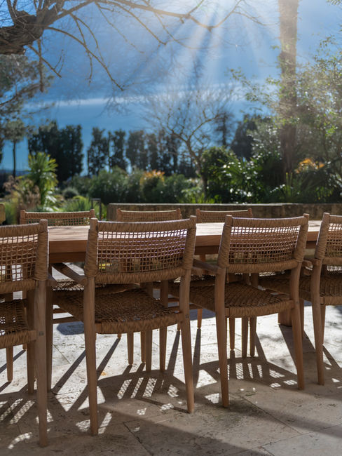 Chaises de salle à manger extérieure en bois et fibres naturelles, éclairées par le soleil dans un jardin provençal.