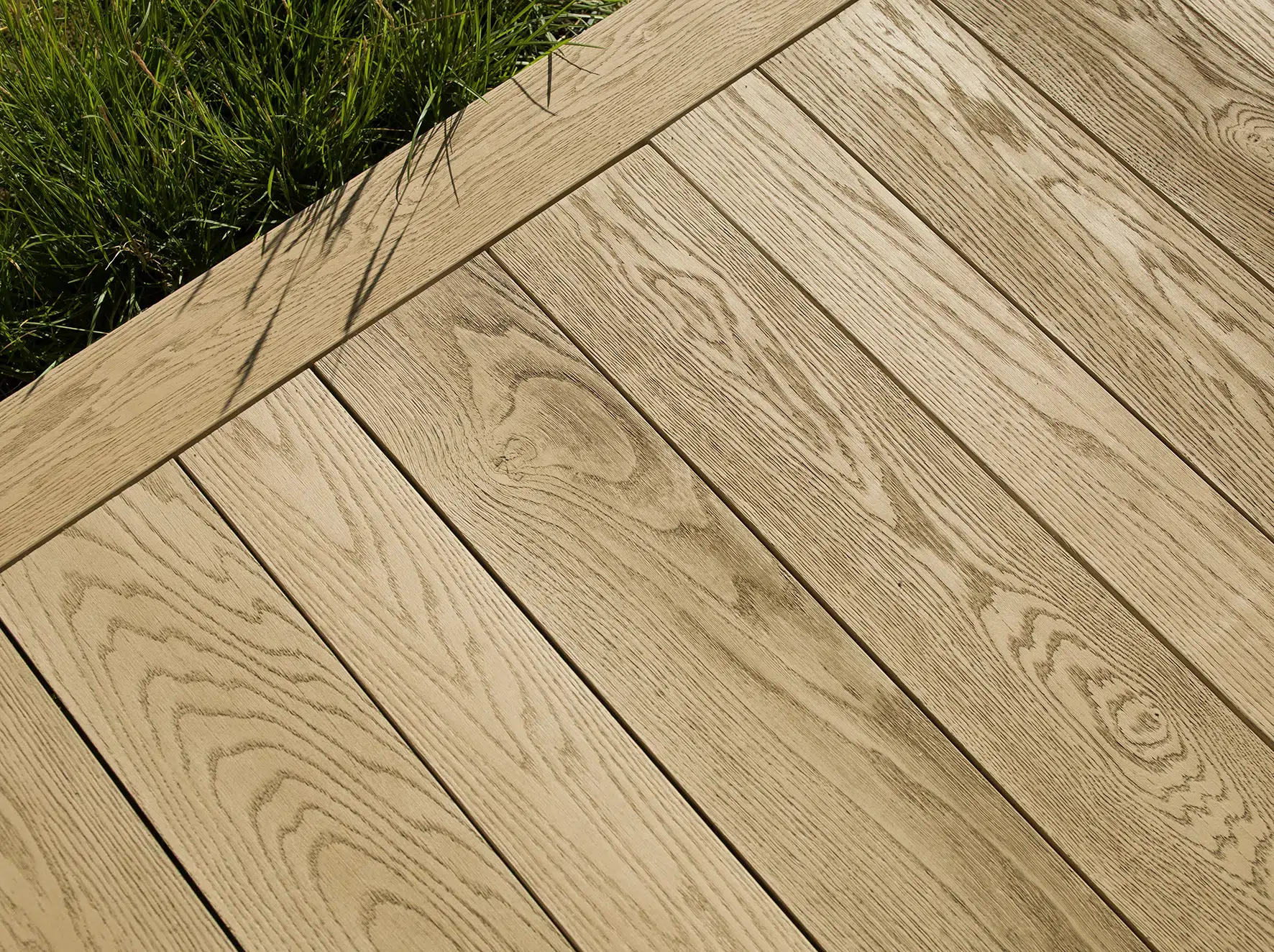 Détail de lames Millboard coloris clair avec veinage bois réaliste, bordées de pelouse.
