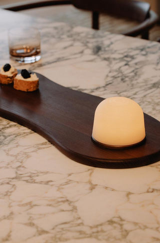 Plateau FONDANT en bois foncé sur une table en marbre, décoré avec une lampe d'ambiance et des bouchées.