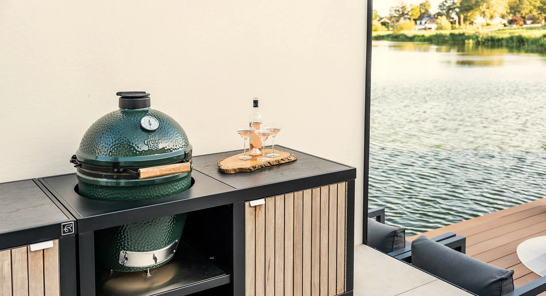 Cuisine extérieure RUBIX Roostr : module avec Big Green Egg encastré, façade à lattes bois et plan de travail minéral, au bord de l’eau.