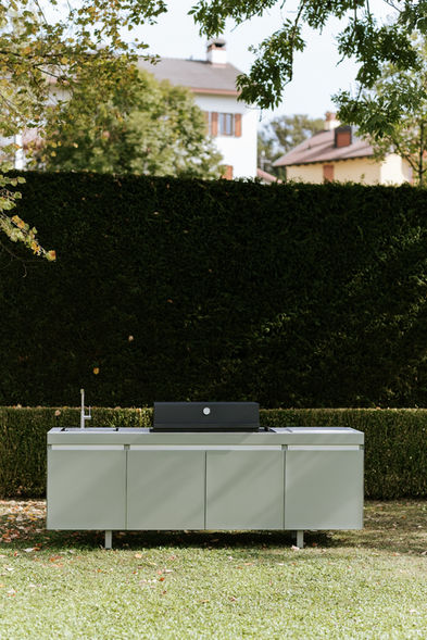 Cuisine extérieure Fogher verte avec évier, barbecue et plan de travail, en situation dans un jardin naturel avec haie taillé