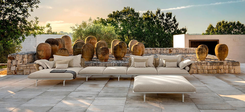 Grand canapé modulaire d’extérieur Cruise Alu avec structure blanche et coussins beiges, installé sur une terrasse en pierre face à des jarres anciennes et une végétation méditerranéenne.