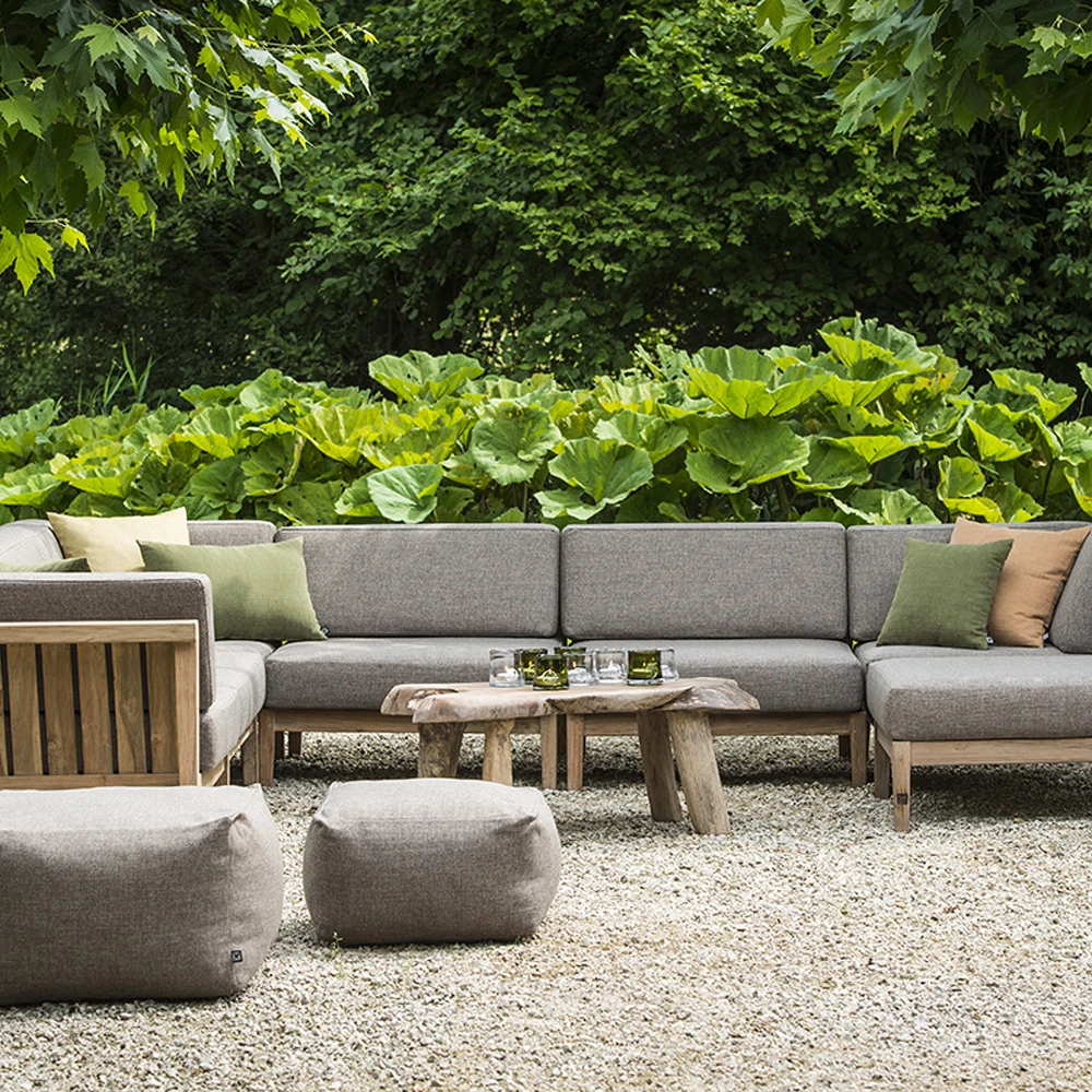 Salon de jardin d’angle en bois et tissu gris, avec table basse rustique et poufs assortis, installé dans un cadre verdoyant