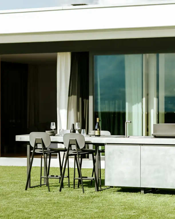 Cuisine extérieure Fogher AGHER avec plan de travail en MDi Pacific Gris, table dressée et bouteille de vin, installée en terrasse dans un cadre contemporain.