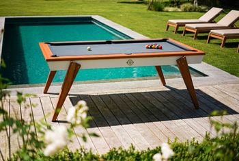 Billard Stella MILLESIME OUTDOOR Blanc installé au bord d’une piscine sur une terrasse en bois