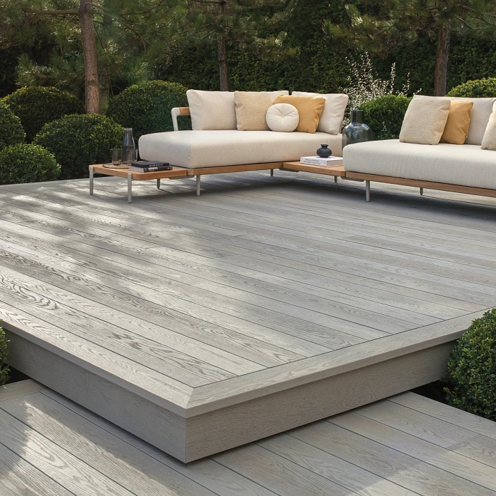 Terrasse Millboard Smoked Oak avec salon d’extérieur haut de gamme entouré de végétation