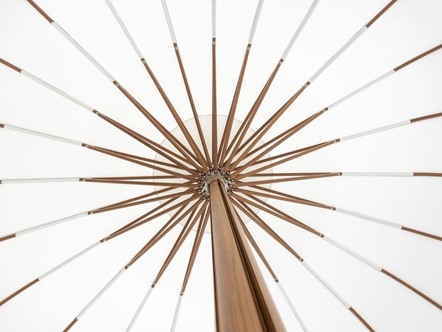 Vue en contre-plongée du mât et des baleines d’un parasol TUUCI, illustrant la structure rayonnante et robuste en finition bois.