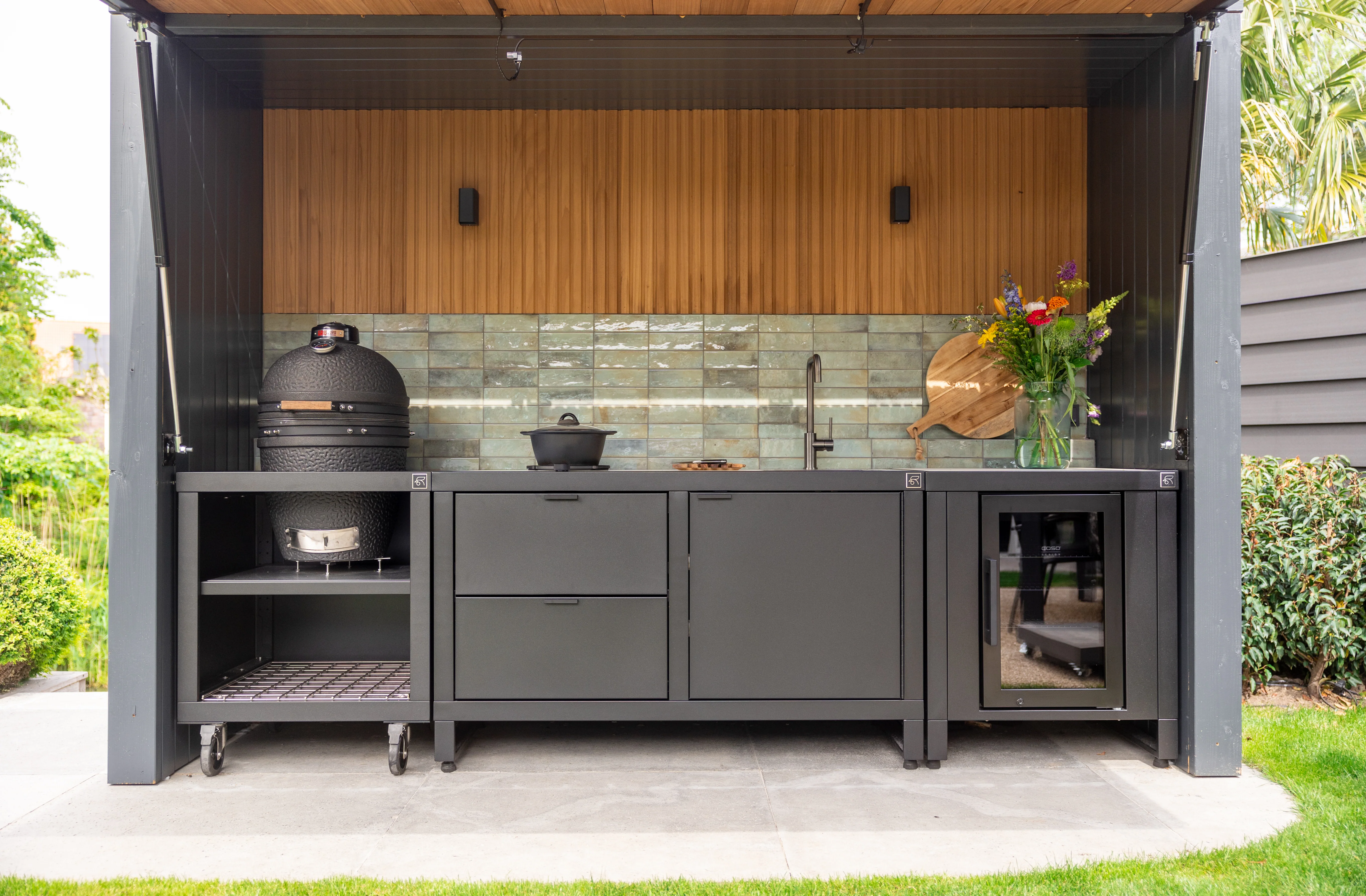 Configuration Rubix complète sous abri : module Kamado à gauche, évier et rangements centraux, réfrigérateur vitré à droite, crédence carrelée.