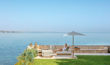 Ambiance balnéaire avec le canapé ITACA Talenti face à la mer, sous un parasol élégant