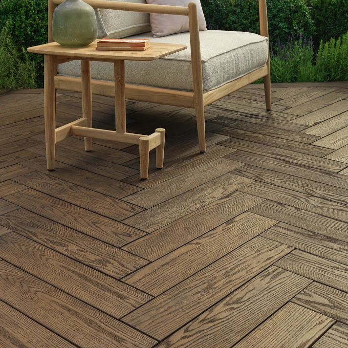 Terrasse avec lames en chevrons finition bois naturel, mobilier extérieur en bois clair comprenant une banquette et une table d'appoint, au cœur d’un jardin paysager verdoyant.