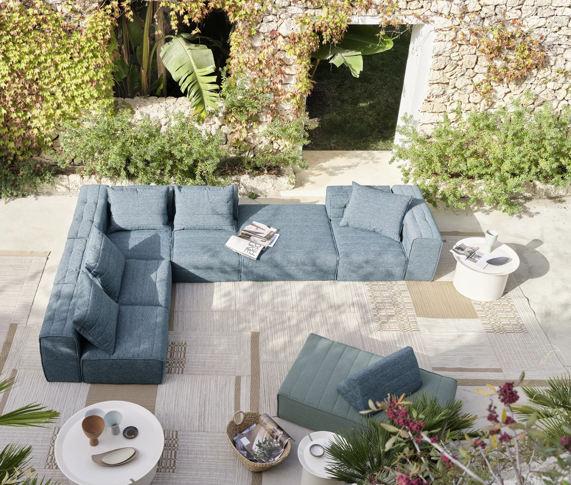 Salon d’extérieur Gervasoni vu du dessus, installé sur un grand tapis patchwork beige et sable, créant une ambiance chaleureuse au cœur d’un jardin méditerranéen.