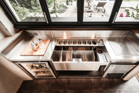 close-up view of the professional outdoor bar's countertop and equipment. The sleek stainless steel workspace includes a refrigerator, ice maker, and various compartments for bar essentials, emphasizing the bar's functionality and modern design