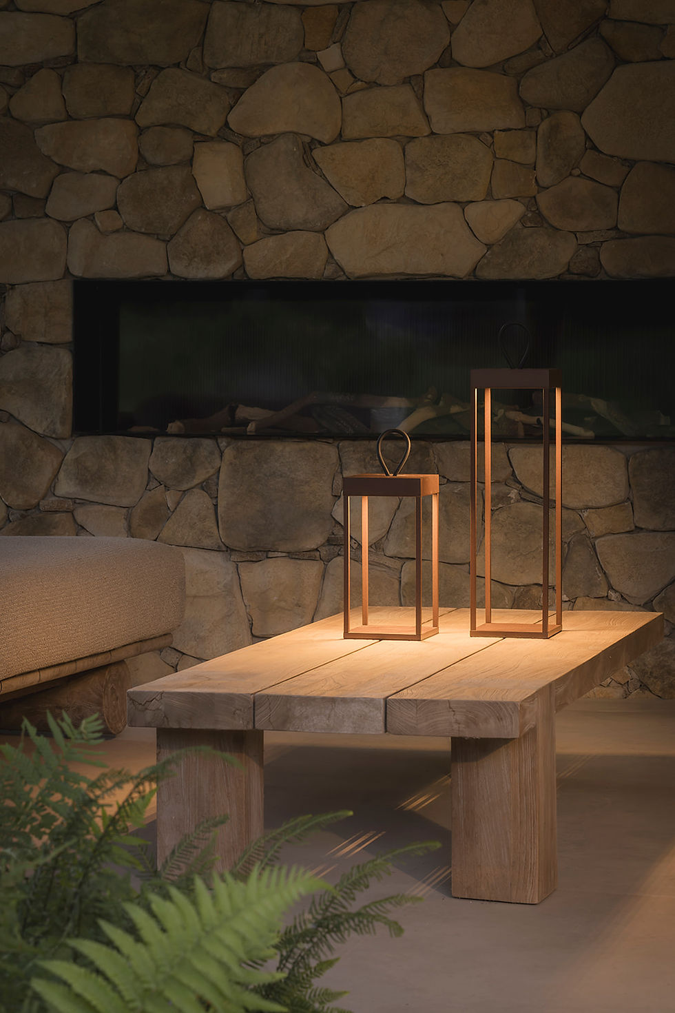 Lanternes BALI 30 QOOZII coloris Corten allumées sur une table basse en bois, cheminée en pierre en arrière-plan