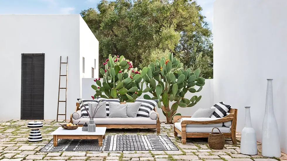 Salon extérieur de la collection JEKO de Gervasoni, composé d’un canapé et d’un fauteuil en teck avec coussins gris et blancs, installé sur une terrasse méditerranéenne entourée de cactus.