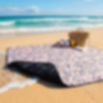 Tapis de pique-nique imperméable à motif confetti rose et multicolore posé sur la plage.