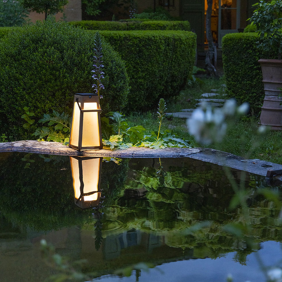 Lanterne solaire Les Jardins posée au bord d’un bassin, lumière chaude se reflétant dans l’eau, haies taillées en arrière-plan — éclairage extérieur haut de gamme sélection WAHO.