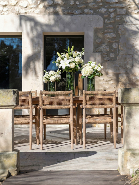 Table extérieure dressée avec bouquets blancs dans vases en verre, devant façade en pierre naturelle.