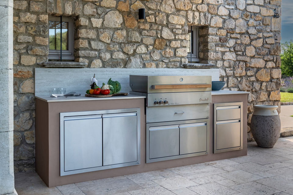Cuisine extérieure sur-mesure avec plancha inox intégrée, installée contre un mur en pierre, alliant matériaux durables et design élégant pour une expérience culinaire en plein air