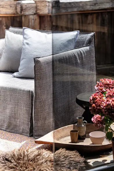 Zoom sur un fauteuil GHOST OUT gris de Gervasoni avec coussins texturés, mis en scène dans un coin chaleureux extérieur.