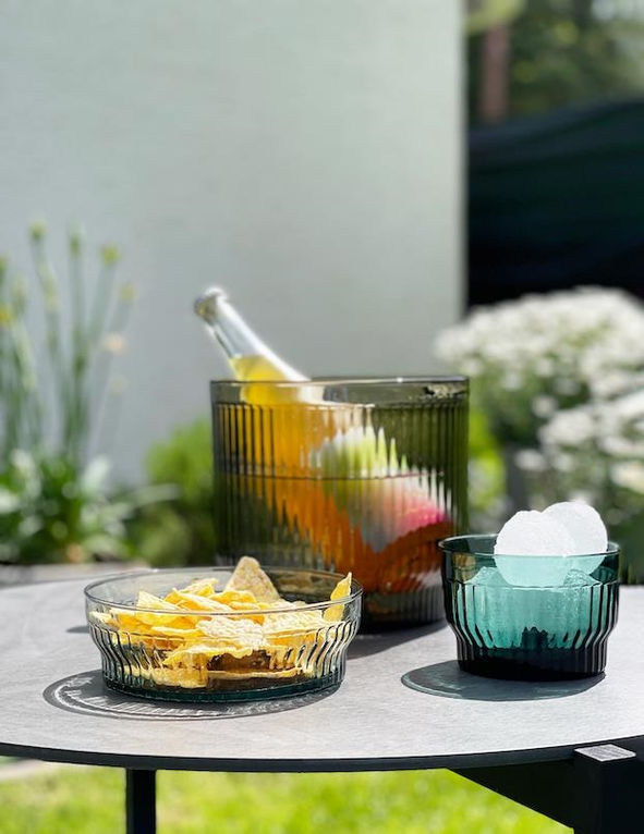 Scène d’été avec un seau à vin LIMA XLBOOM rempli de boissons colorées, accompagné de coupelles de chips et glaçons en verre