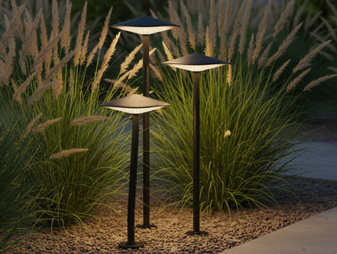 Groupe de trois lampes Kinno allumées, intégrées dans des graminées ornementales en jardin contemporain.