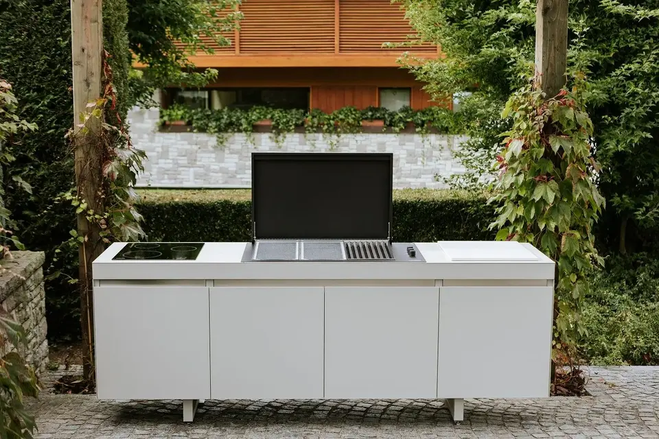 Cuisine extérieure modulable blanche avec barbecue intégré, plaques de cuisson et rangements fermés, offrant une solution élégante et fonctionnelle adaptée à tout espace extérieur.