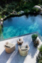 Mobilier de jardin : deux fauteuils tressés et table bois sur terrasse au bord d’une piscine naturelle turquoise