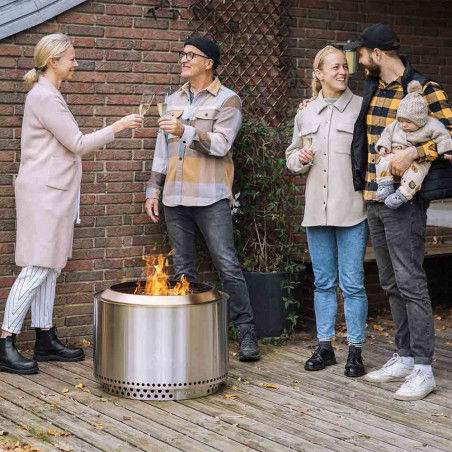 Un groupe d’adultes avec un bébé profite d’un moment convivial autour du brasero Yukon Solo Stove sur une terrasse en bois.