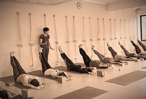 Tara Duffy teaching Urdhva Prasarita Padasana to students in a yoga class sepia filter.