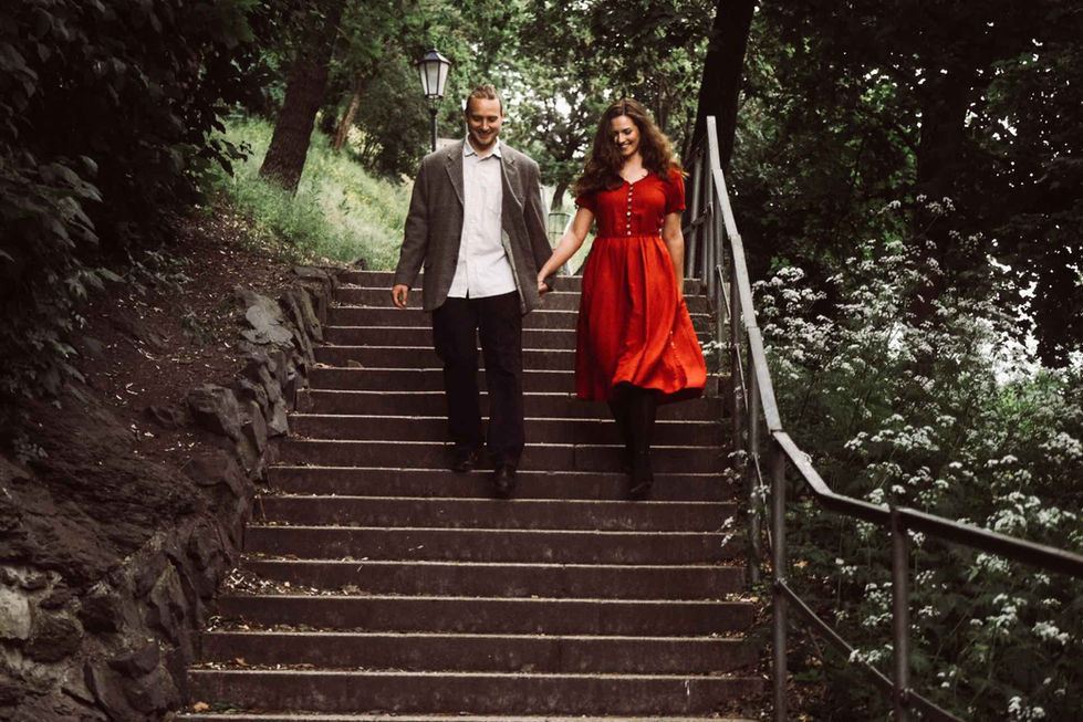 Pár držící se za ruce při chůzi po schodech v parku, žena v červených šatech.