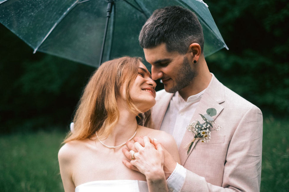 Nevěsta a ženich pod deštníkem, drží se a dívají se na sebe.