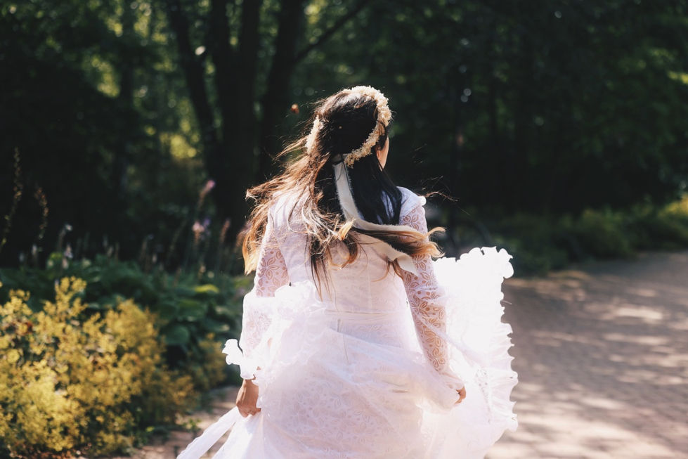 Nevěsta v bílých šatech běží přírodní zahradou za slunečního svitu.