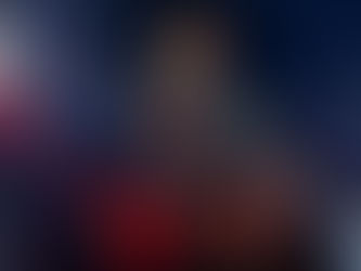 Person in an orange beanie and jacket smiles while sitting in a specialized wheelchair at night. A bright light shines in the background.