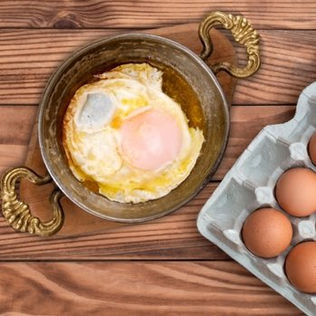 Doğal köy yumurtası ve tereyağıyla pişirilmiş sahanda yumurta, sıcak tavada servis edilirken çekilmiş fotoğraf.