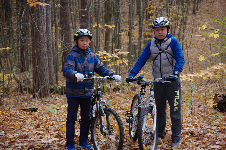 Two Asian children standing with bikes in a forest area