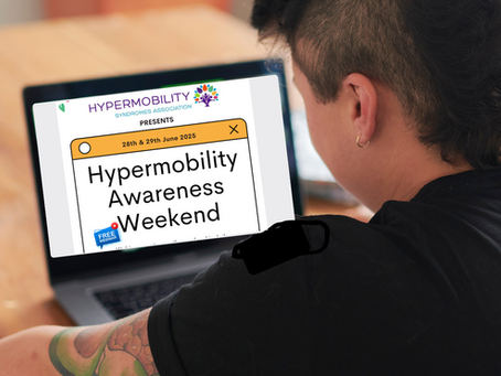 Person with short dark hair reading a laptop screen that shows the Hypermobility Syndromes Association logo, then 28th-29th June 2025. Hypermobility Awareness Weekend