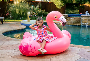 Little girl sitting on giant pink flamingo pool float at backyard party – Gumball Entertainment inflatable rentals DFW