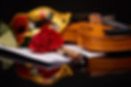 Violin (fiddle), theater mask and red rose lying on the sheet of music on a black backgrou