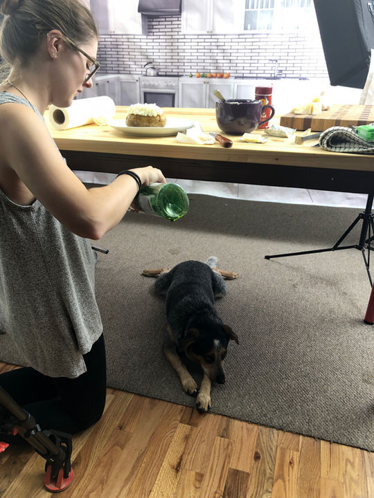 Woman adjusts food with dog watching under table