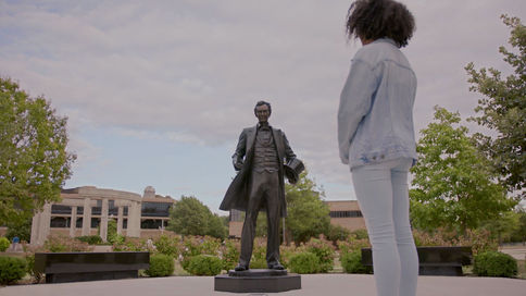 UIS Student stands contemplatively in front of Abe Lincoln statue at UIS campus