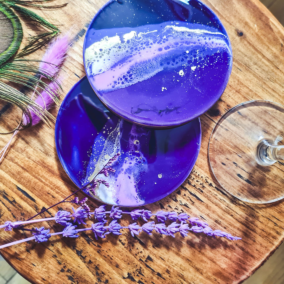 Two purple resin coasters reflecting a super shiny gloss on the surface. Surrounded by beautiful purple flowers.