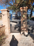 Brick pillars and gate with a sunlit path and trees visible.