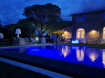 Nighttime view of a pool with people and a stone house as background.