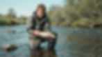 Man kneeling in river holding a fish